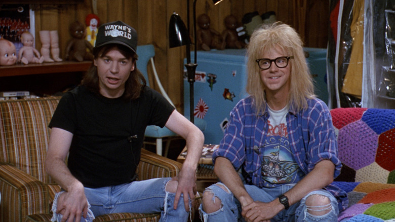 Wayne and Garth sit in their basement on the couch talking into a camera.