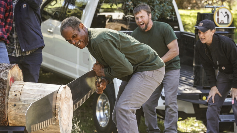 A contestant saws a log as players cheer him on in Tough as Nails (2020)