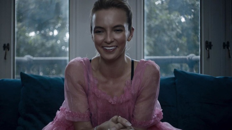 Villanelle (wearing a tulle, bubblegum pink dress) sitting on a therapists's couch, laughing in "Killing Eve"