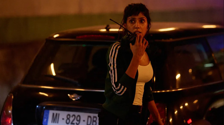 Zara talks into a radio in front of a car in "Paris Has Fallen" (2024)