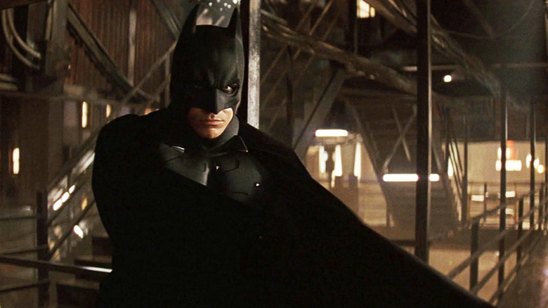 Batman sits with his cape covering him in Batman Begins (2005)