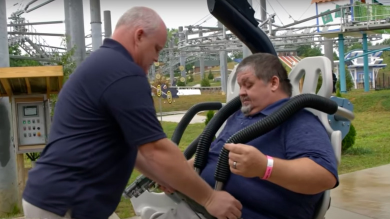 An amusement park employee helps secure Chris in his seat