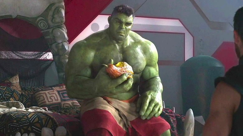 The Hulk with a towel around his waist sitting on a bed and eating fruit while talking to Thor in Thor: Ragnarok