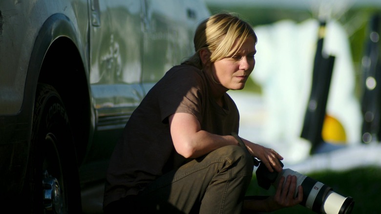 Lee crouches behind a car with her camera in "Civil War" (2024)