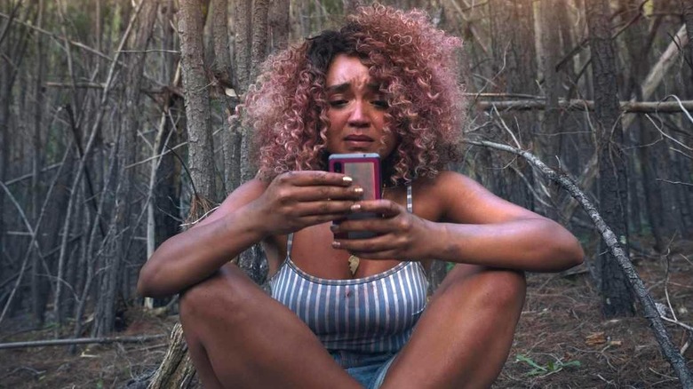 Upset Aisha Dee looks at phone in the woods