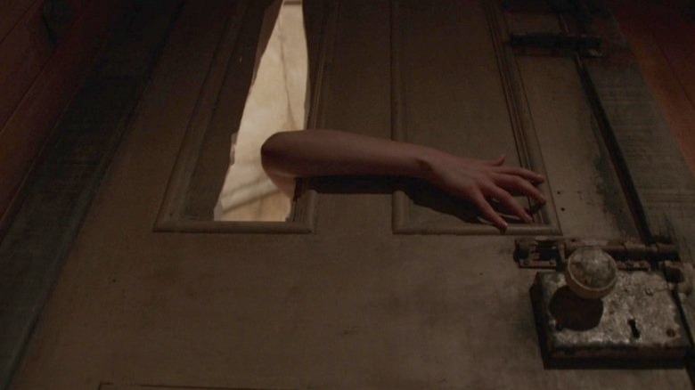Lorraine reaching her arm through a hole in the door