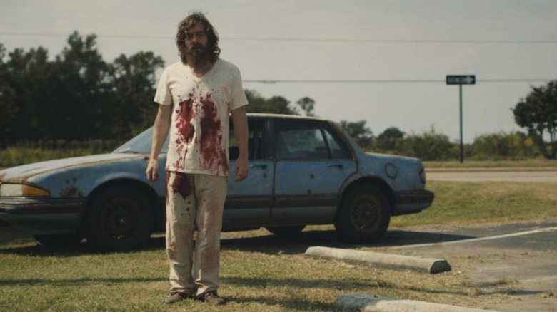 A bloodied Dwight Evans stands next to his Pontiac in "Blue Ruin" (2013)