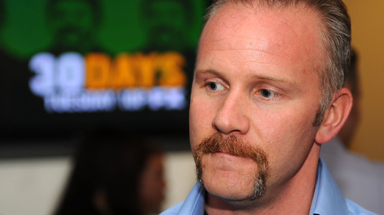 Morgan Spurlock thinks in front of blurred TV screen