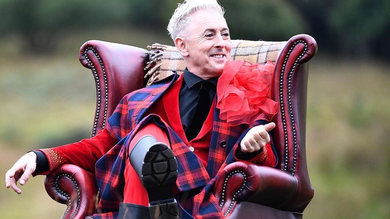 Alan Cumming hosting The Traitors in a red armchair