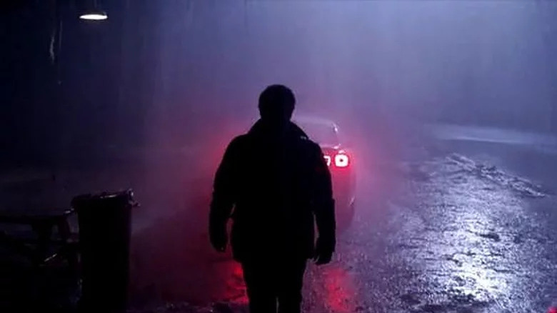 Silhouetted man standing behind car 