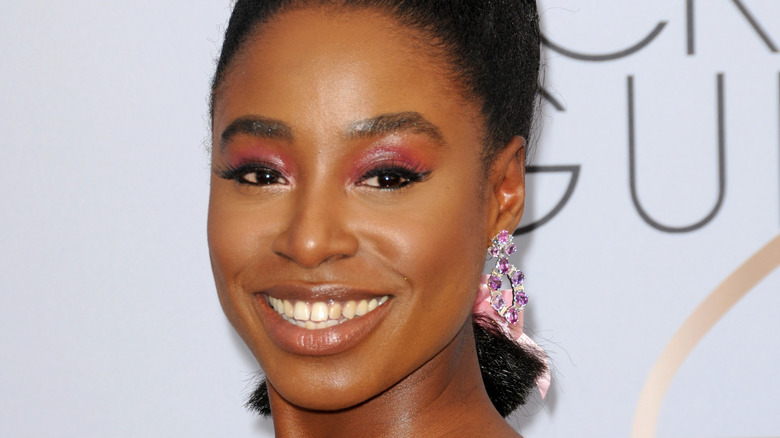 Kirby Howell-Baptiste smiling with purple earrings and a pink bow