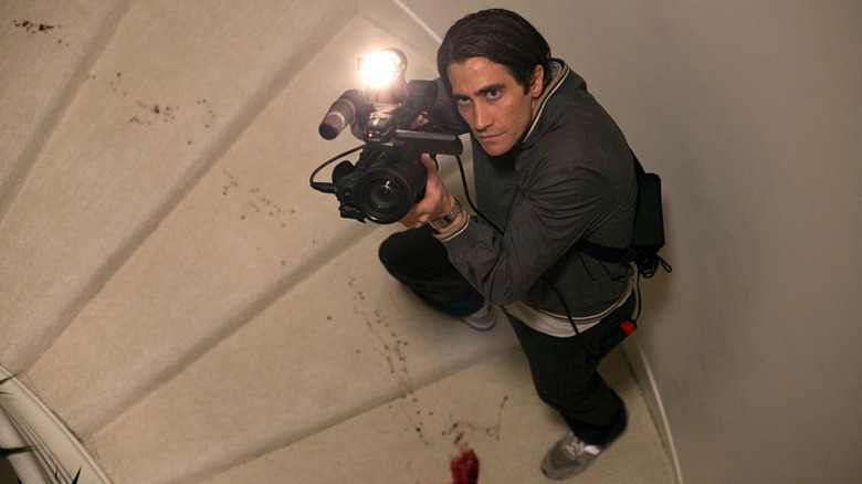 Lou walks up bloody stairs with a camera in "Nightcrawler" (2014)