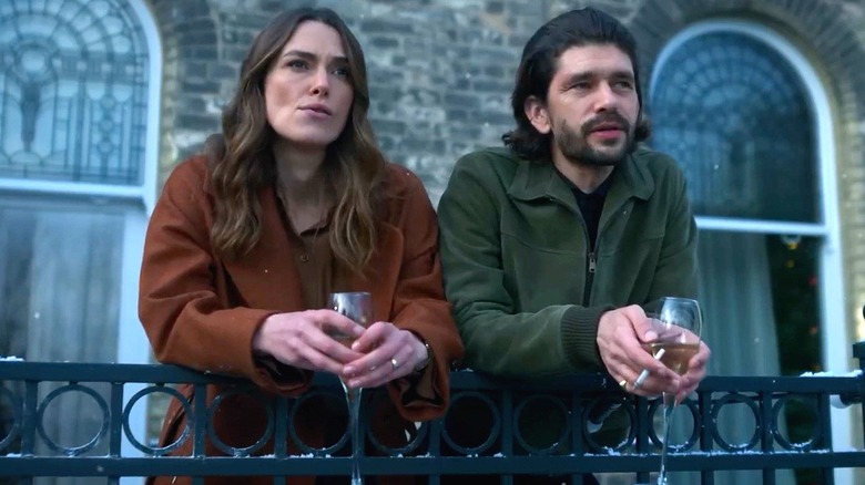 Webb and Young lean against a balcony railing, holding wine glasses.