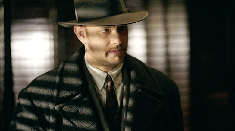 Michael Sullivan stands in the striped light of a window shade, looking out from under the brim of a fedora in "Road to Perdition" (2002)