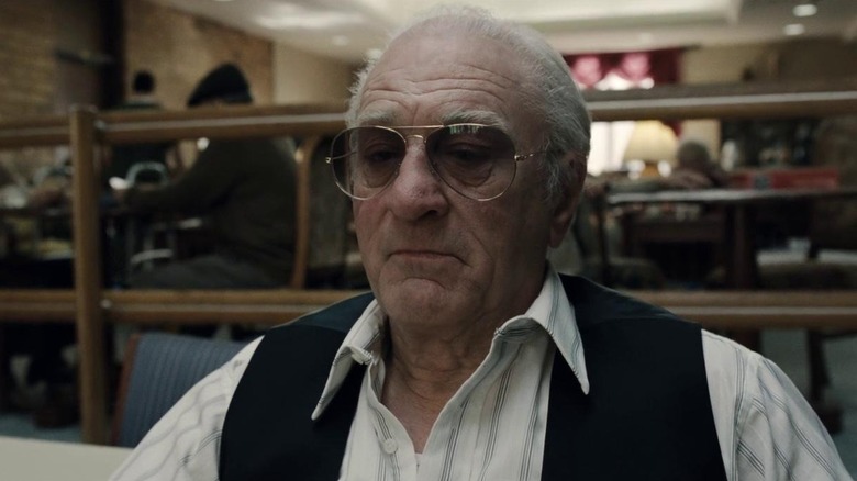 An aging Frank Sheeran sits quietly at a table in a restaurant, looking pensive in "The Irishman" (2019)