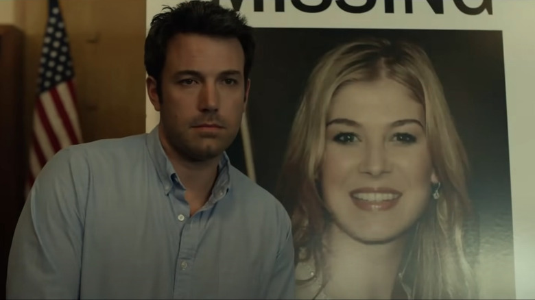 Ben Affleck standing in front of a poster of Rosamund Pike in Gone Girl