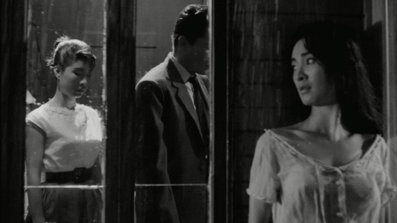 A woman hides outside a window to a room with two people in The Housemaid (1960)