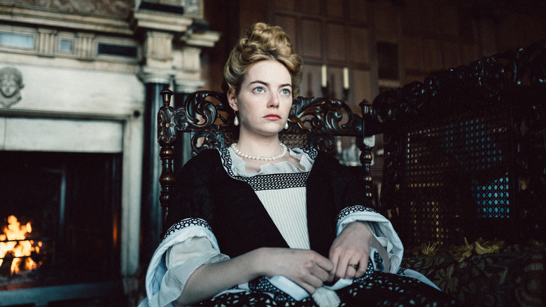 Emma Stone as Abigail sitting in front of a fireplace in The Favourite (2018)