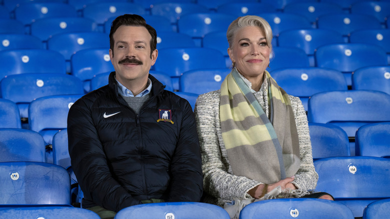 Ted and Rebecca sit together in blue stadium seats