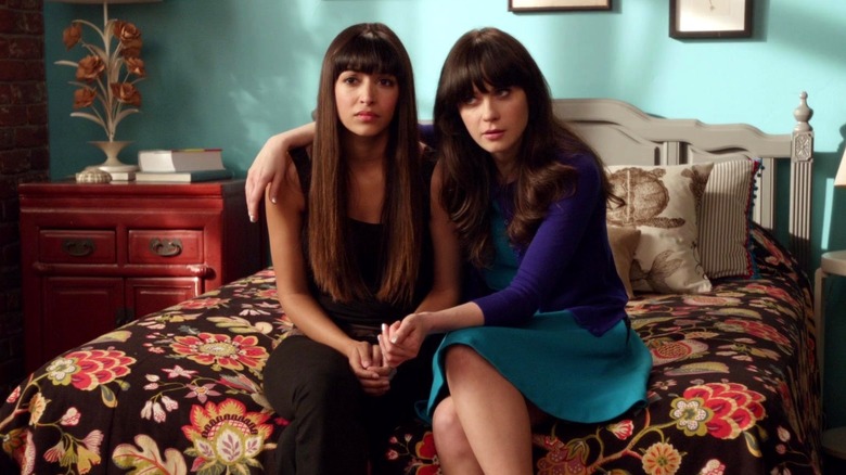 Jess and Cece sit together on the edge of a bed