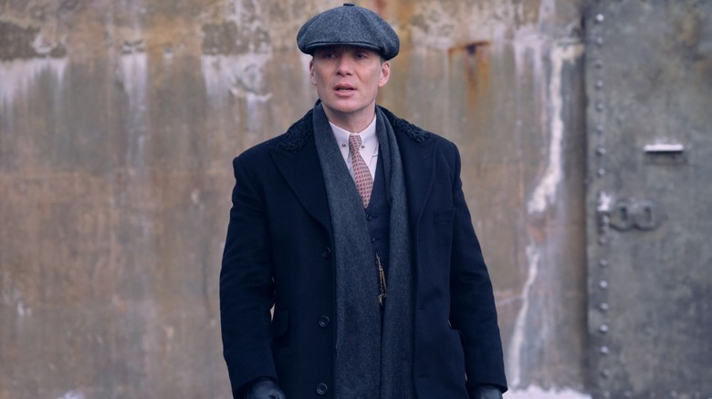 Tommy Shelby walks outside in a hat, coat, gloves, and scarf