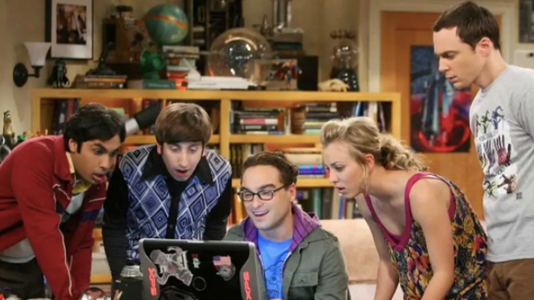 Penny and the guys look at laptop in living room