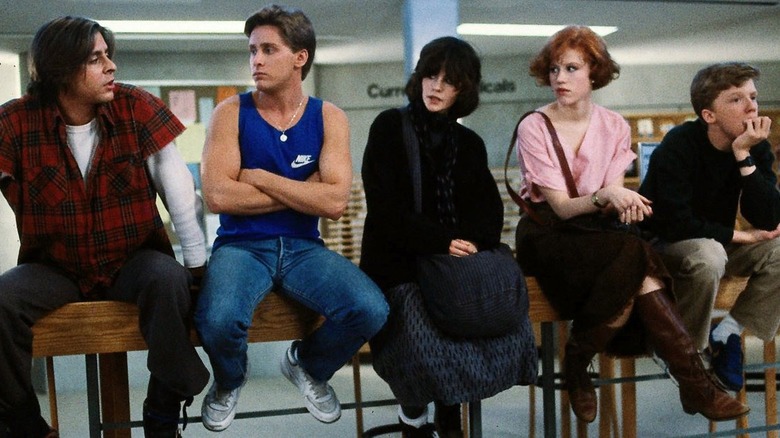 The cast of The Breakfast Club sit on a desk