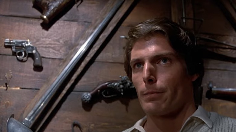 Christopher Reeve in front of a wall of weapons