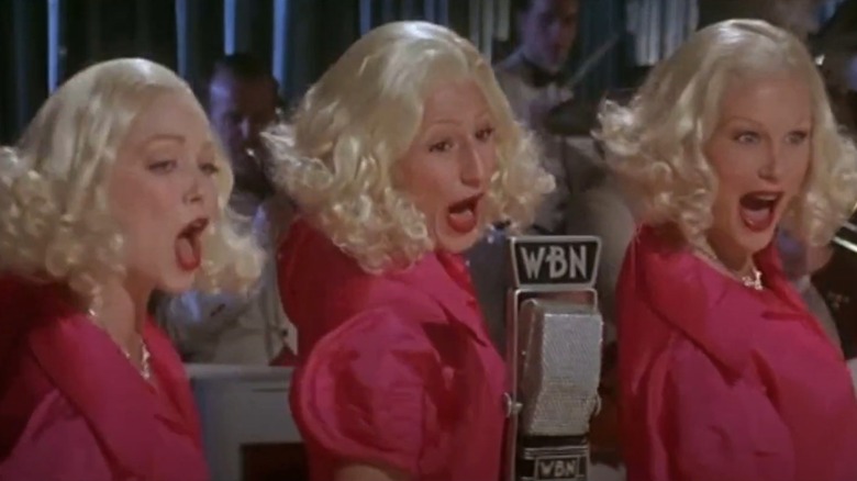 Three blonde performers sing into a mic