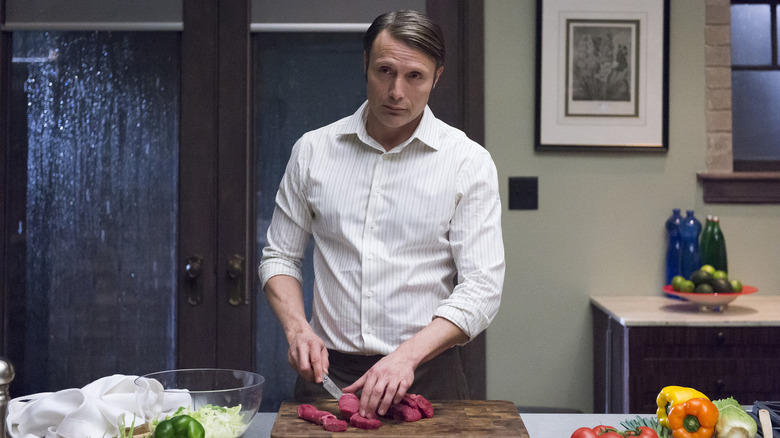 Hannibal chopping meat in his kitchen 