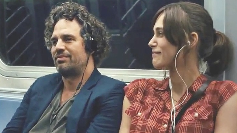 Dan and Gretta sit together on the subway, each listening to headphones and smiling