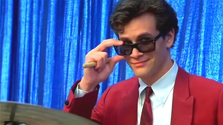 Tom Everett Scott wearing a red suit and looking over sunglasses, smiling