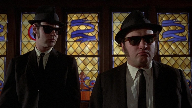 Jake and Elwood Blues stand in front of a stained glass window
