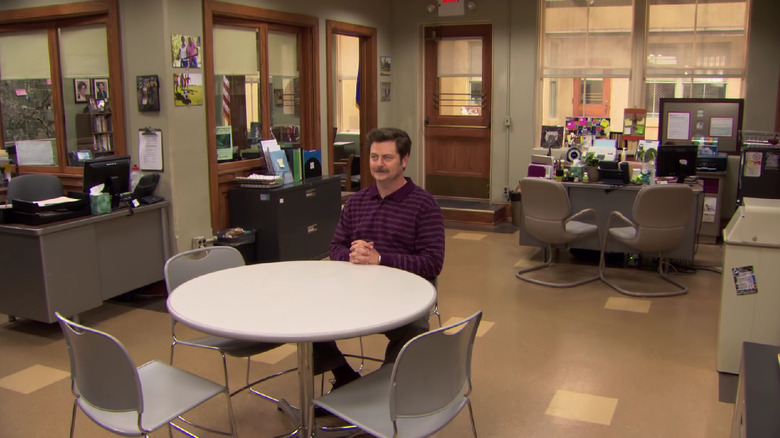 Ron Swanson sits and smiles alone in an empty office