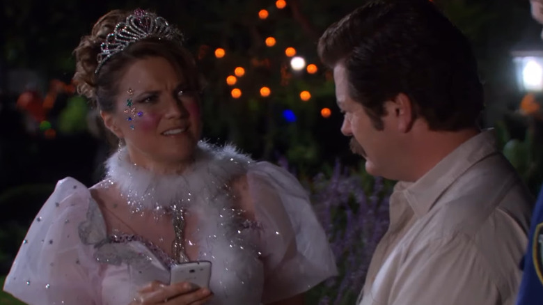 A confused Lucy Lawless dressed as a princess looks past Ron Swanson