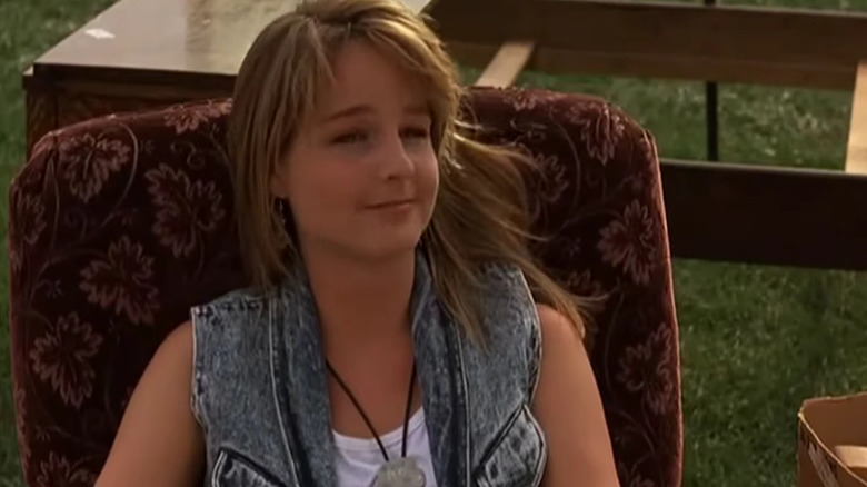 Helen Hunt sits in a chair outside and smirks