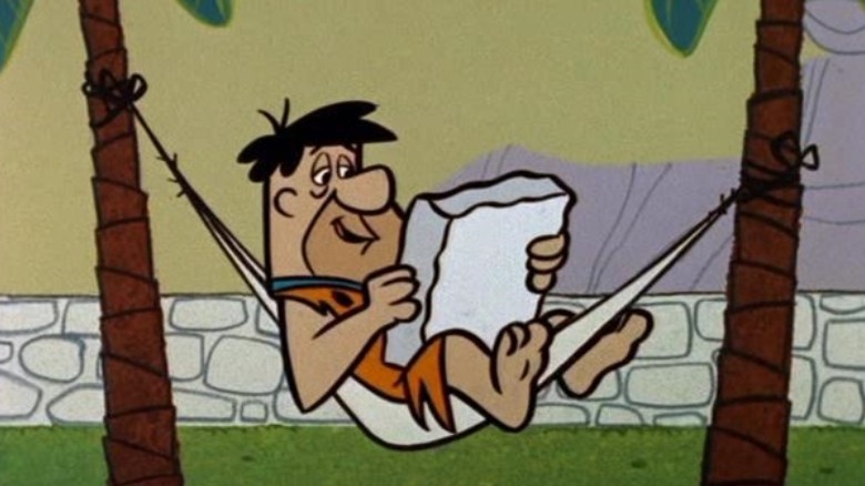 Fred Flintstone reads in his hammock