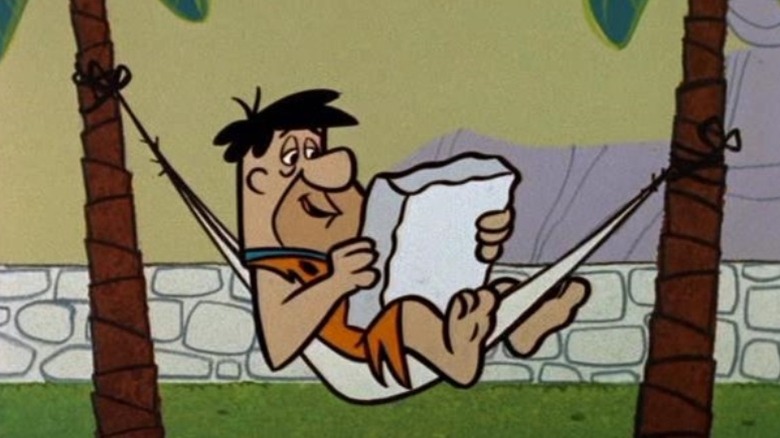 Fred Flintstone reads in his hammock