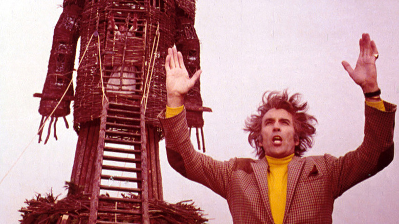 Christopher Lee holds up arms in front of wicker effigy