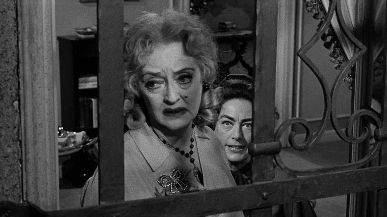 Bette Davis sad looks out window with angry Joan Crawford behind her