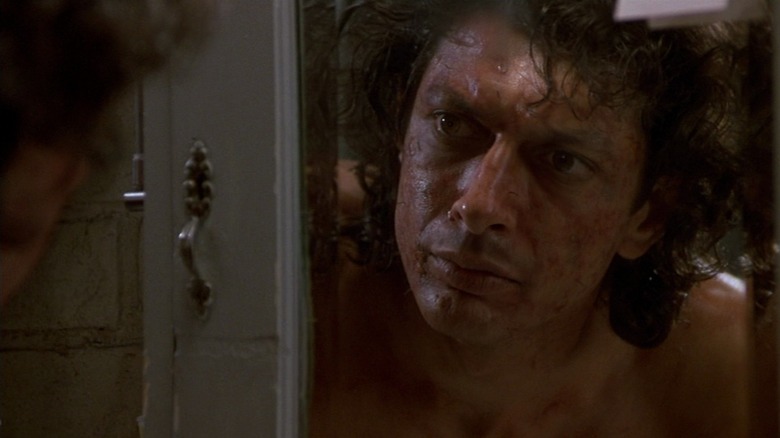 Seth Brundle (Jeff Goldblum) examines his mutating face in the mirror in 1986's The Fly