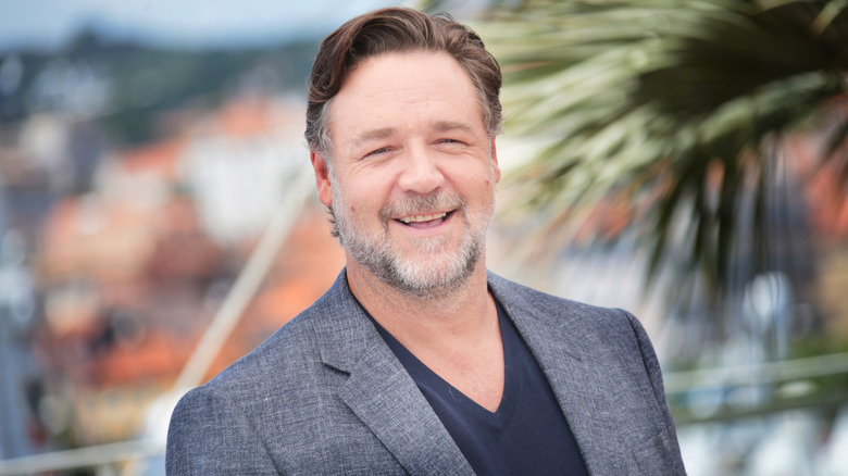 Russell Crowe smiling in front of a palm tree