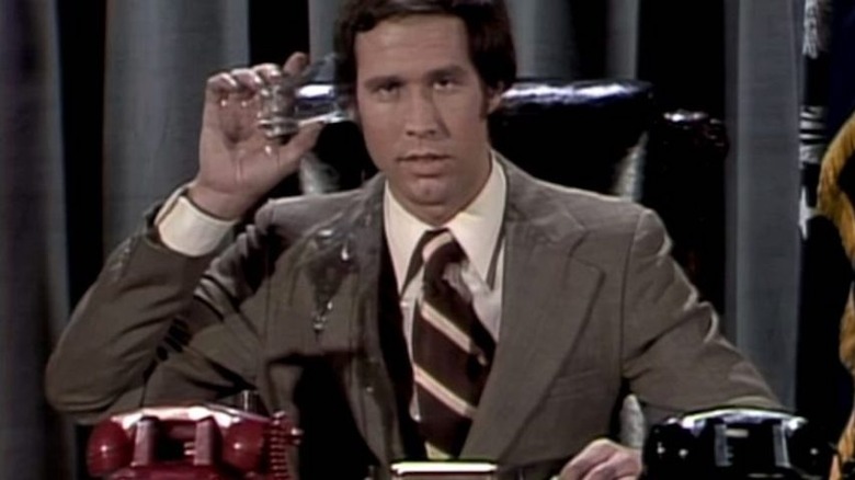 Chevy Chase puts a cup to his ear