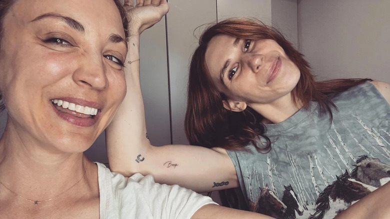 Kaley Cuoco and Zosia Mamet smiling and flexing their arms