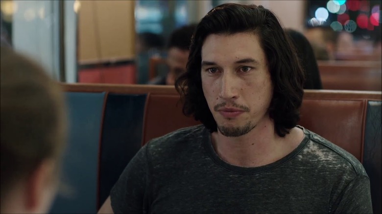 Adam Driver seated and staring