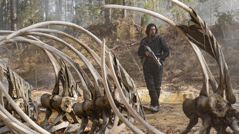 Adam Driver stands near a dinosaur skeleton