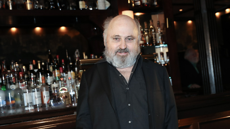 Clark Middleton stands and smiles in front of a bar