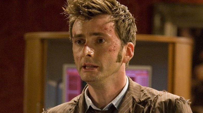 The Tenth Doctor covered in scratches and bruises, with a blank, exhausted stare on his face