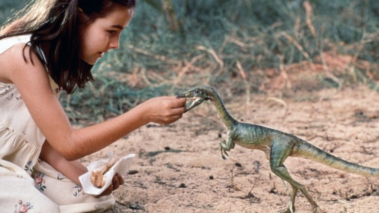 A little girl feeding lunch meat to a small green dinosaur