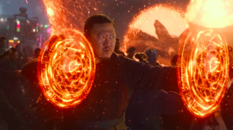 Wong summons magical energy around his hands while superheroes and Wakandan troops appear through portals behind him